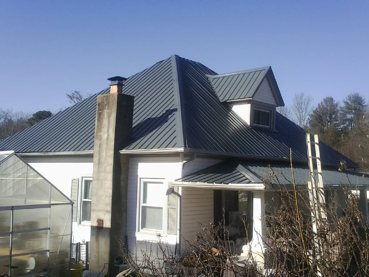 Dark blue standing seam metal roof on a white farmhouse with dormer — Slate & Tile Roof Repair by Roofing Brothers in Vass