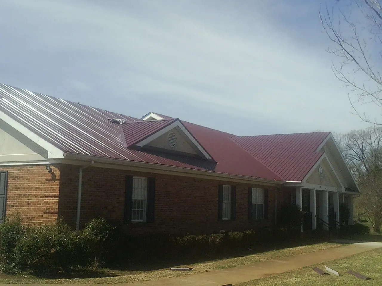 Red metal roof with gabled entries on a long brick building, from a Hail Damage Roof Repair job in Vass