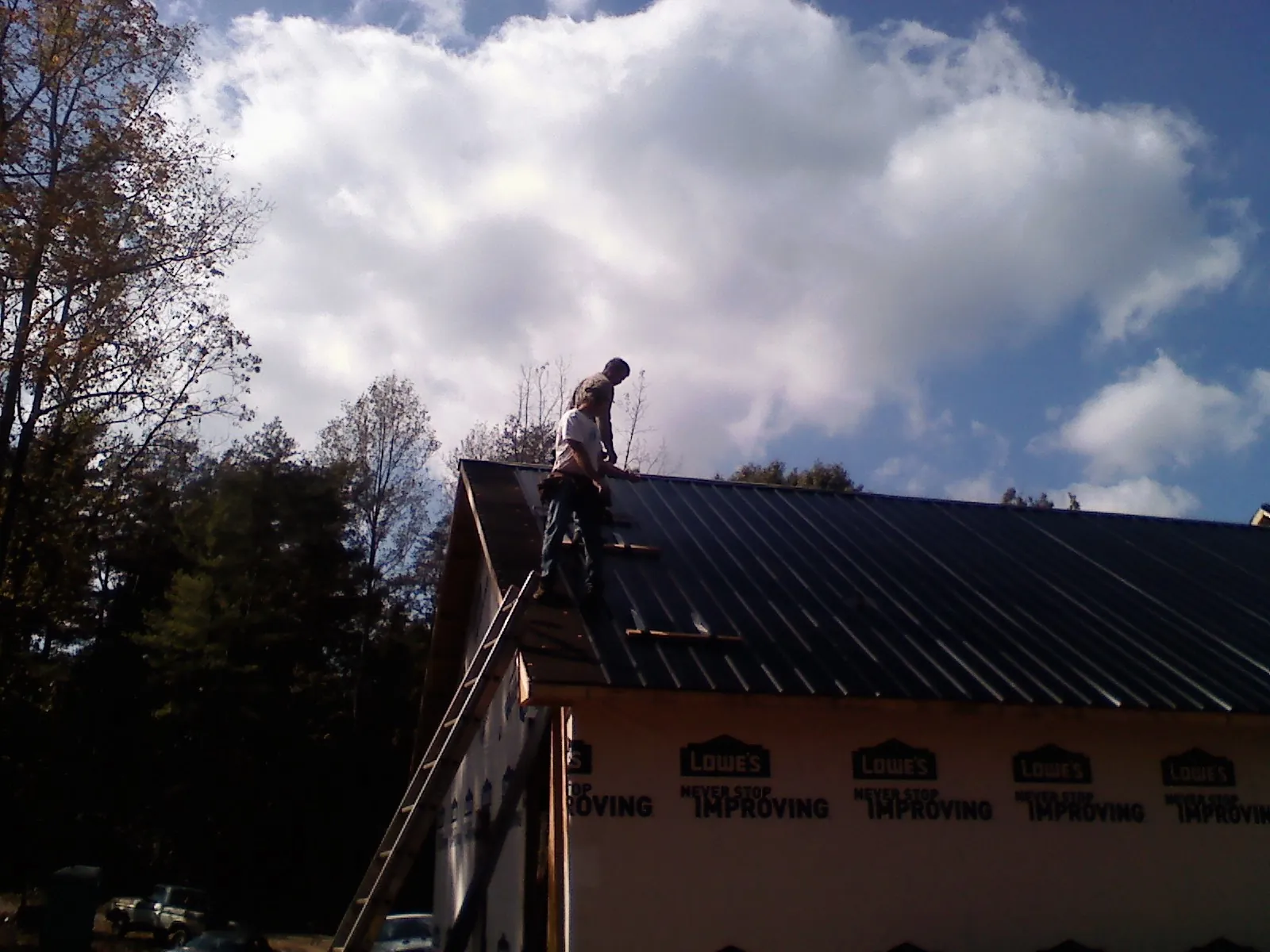 Roofer fastening dark metal panels high against a cloudy sky, from a Roof Inspection job in Vass
