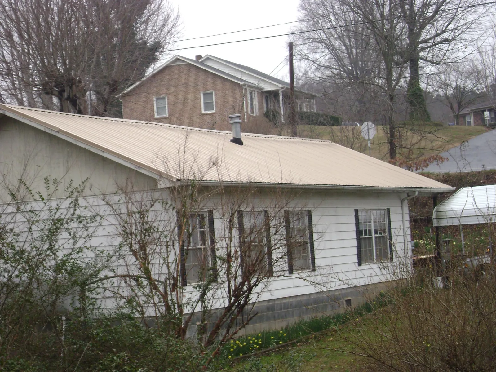 Tan metal roof on a white sided house set into a hillside — Commercial Roofing by Roofing Brothers in Vass